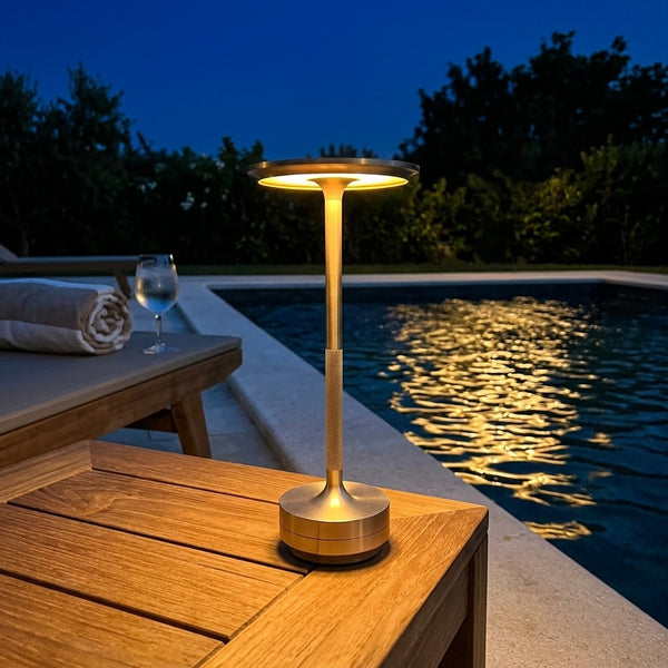 Gold water resistant Eclara Ilumina cordless lamp glowing beside a swimming pool at night with warm reflections on the water