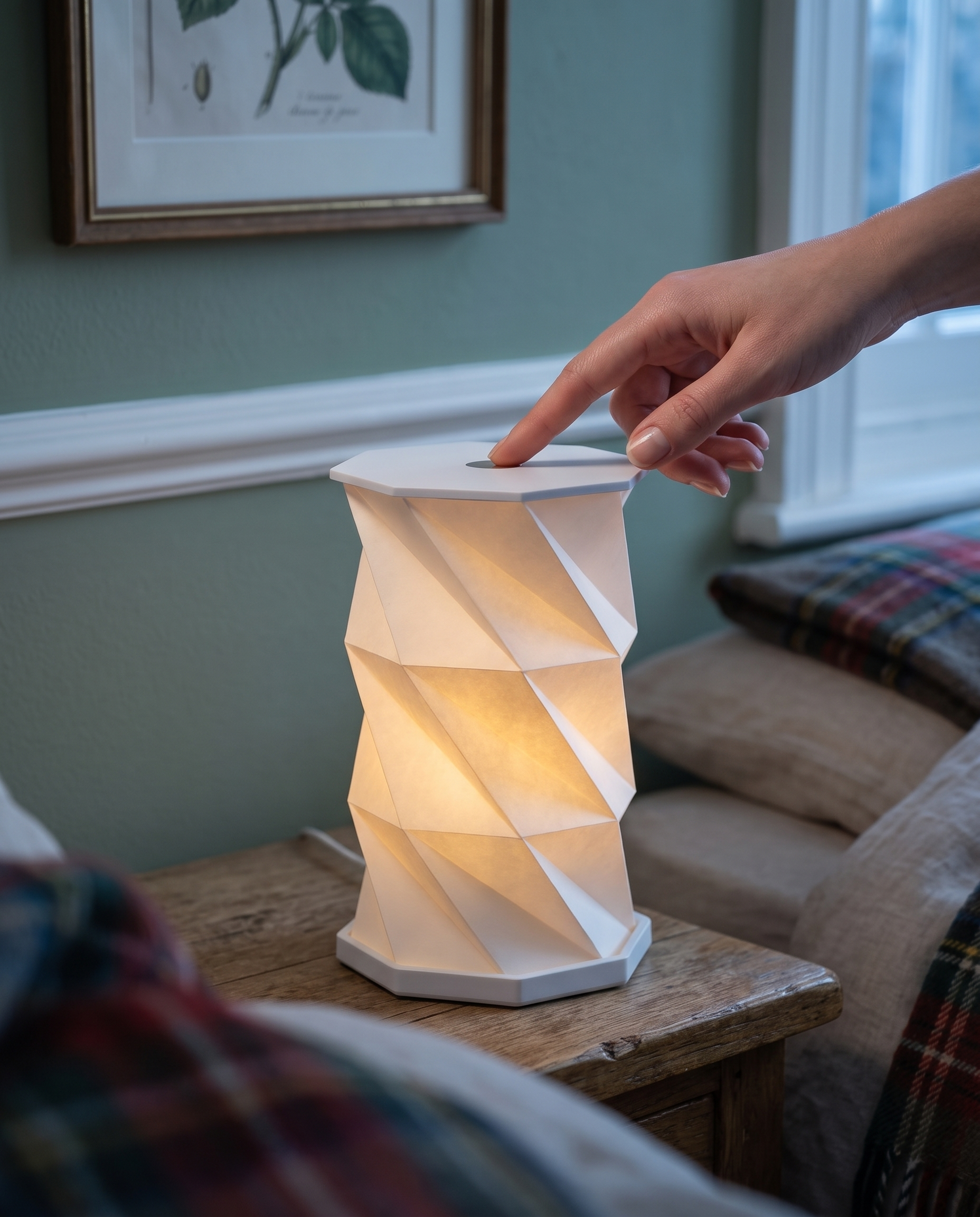 A hand tapping the top touch panel of the Lumina Fold lamp